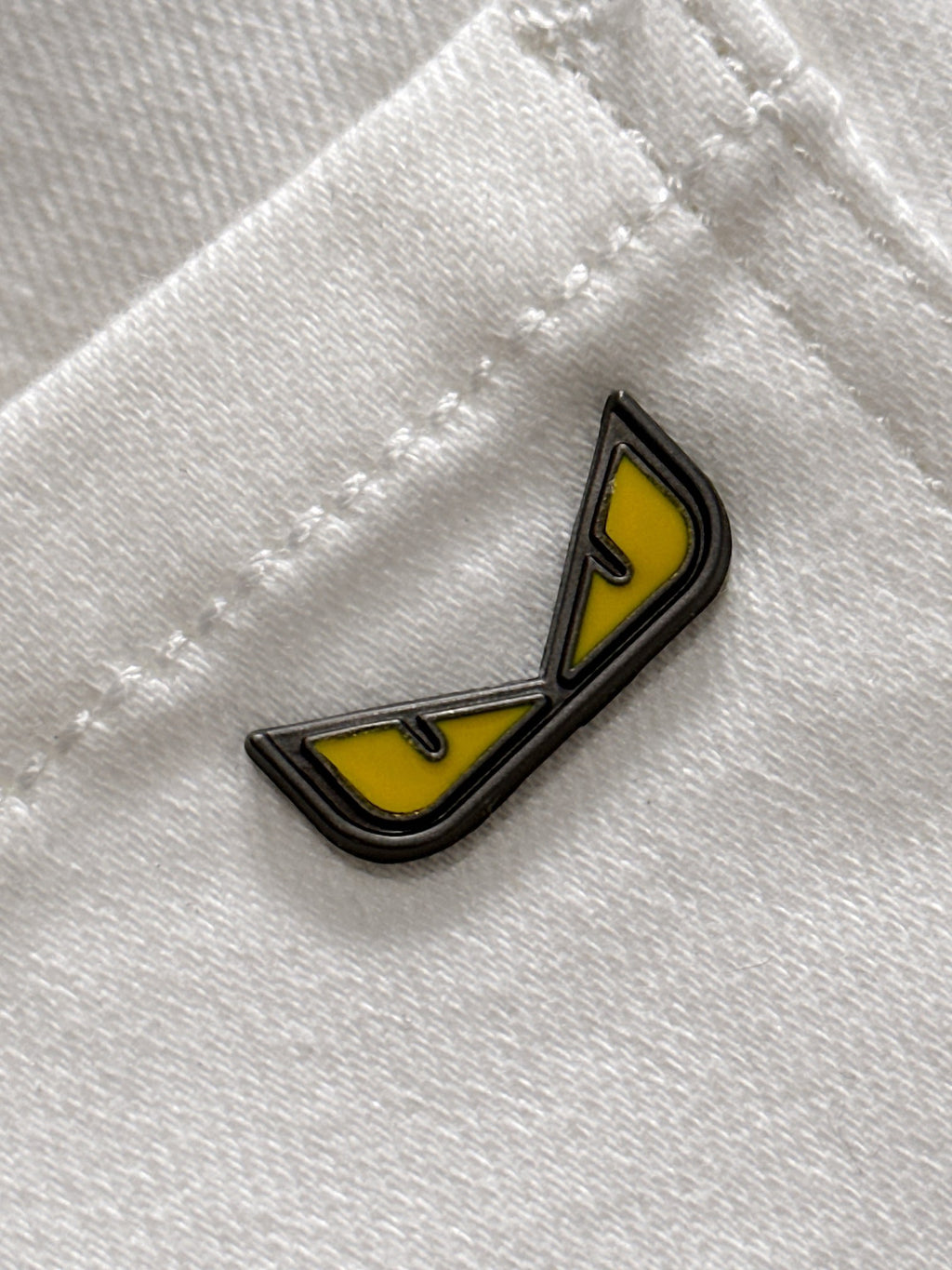 Yellow and black enamel logo patch on white denim fabric