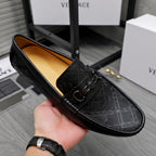 Black leather slip-on loafer held in hand; textured upper and buckle strap visible.