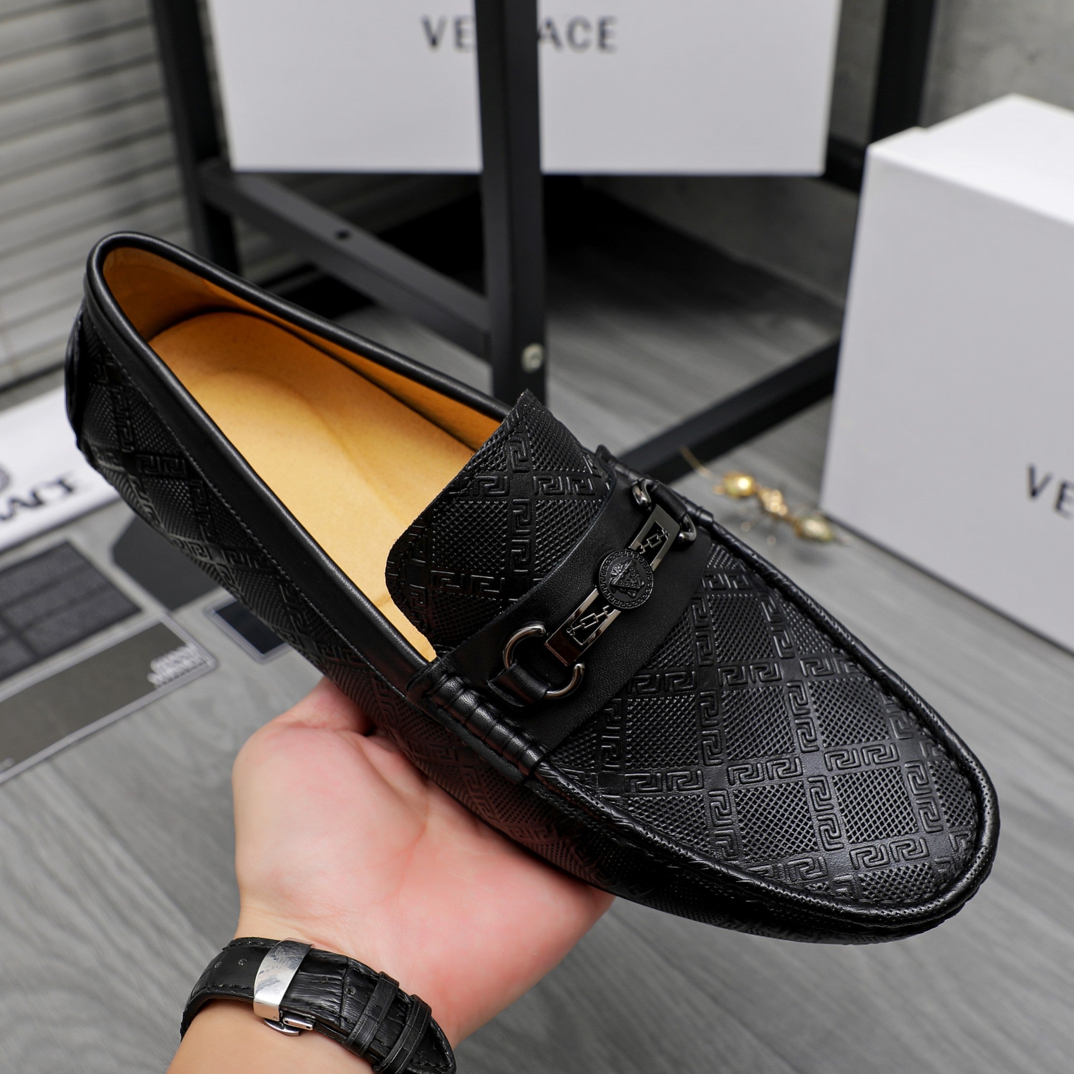 Black leather slip-on loafer held in hand; textured upper and buckle strap visible.