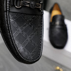 Close-up of black loafer upper with embossed geometric pattern and metal buckle strap.