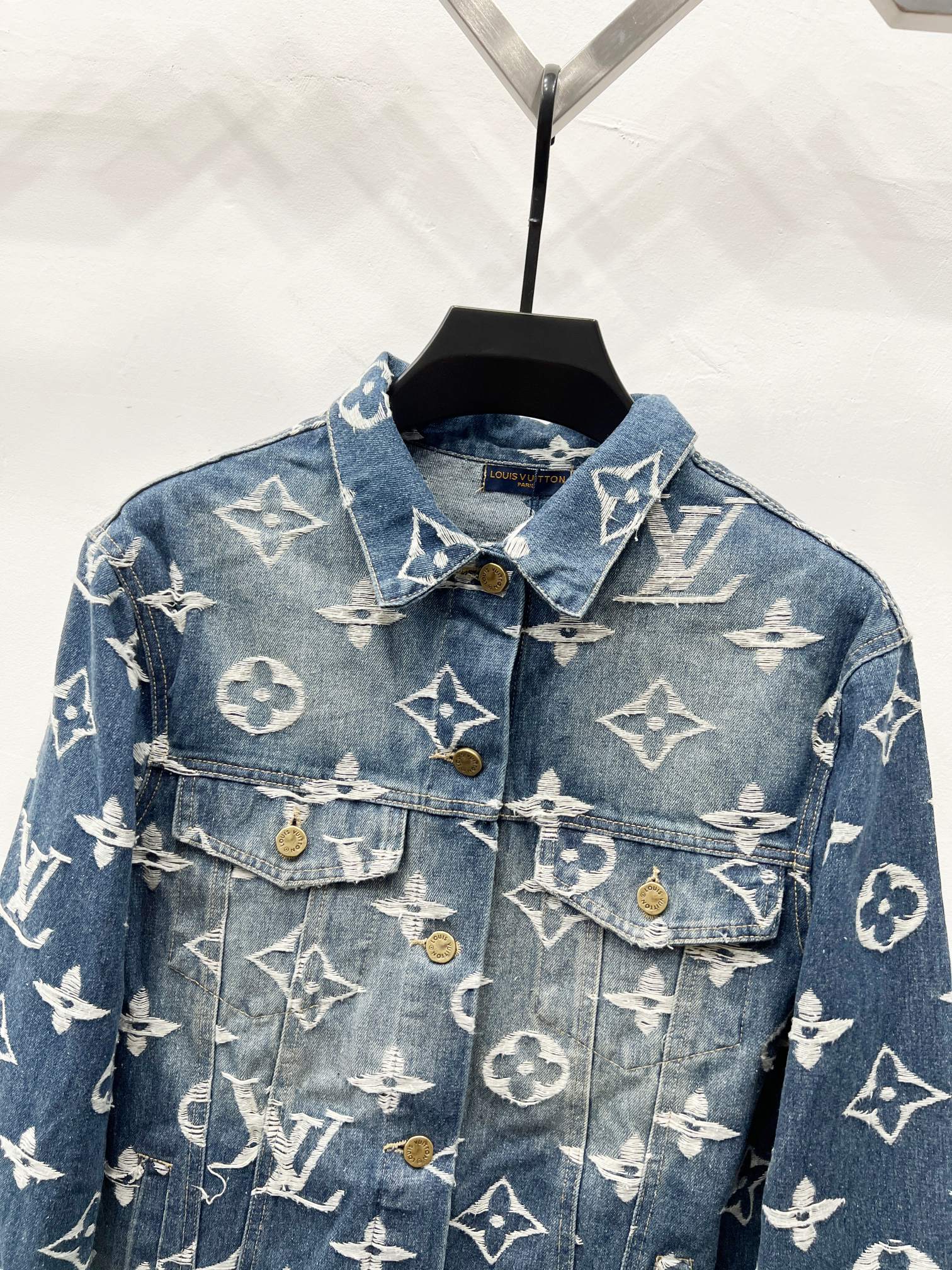Blue denim jacket front with white monogram pattern, flap pockets and gold buttons
