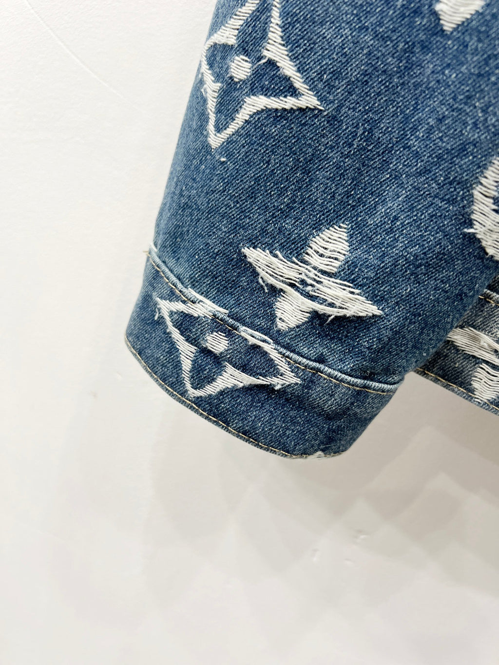 Blue denim jacket sleeve with white monogram pattern and stitched cuff