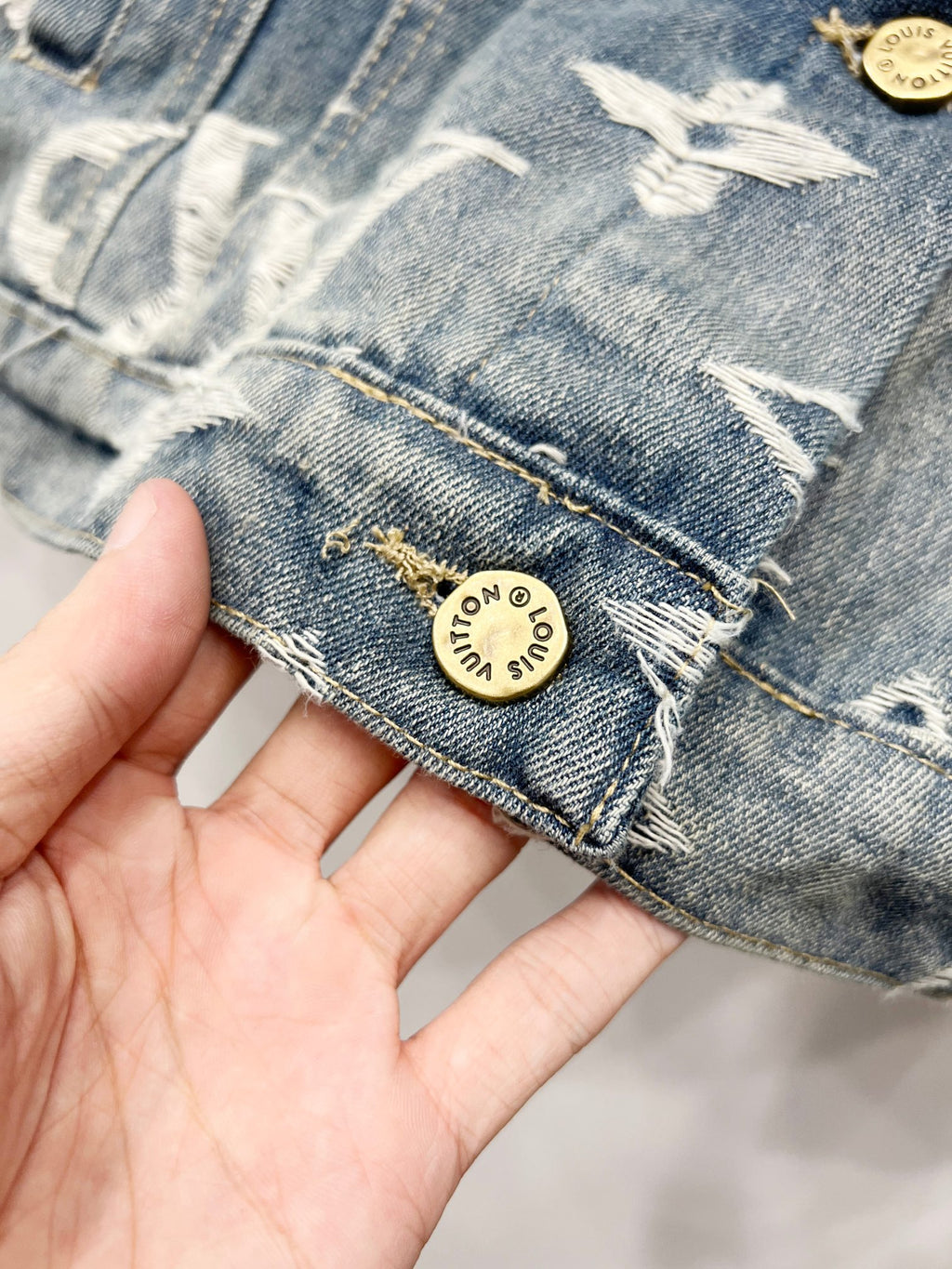 Blue denim jacket cuff with white monogram stitching and round gold logo patch