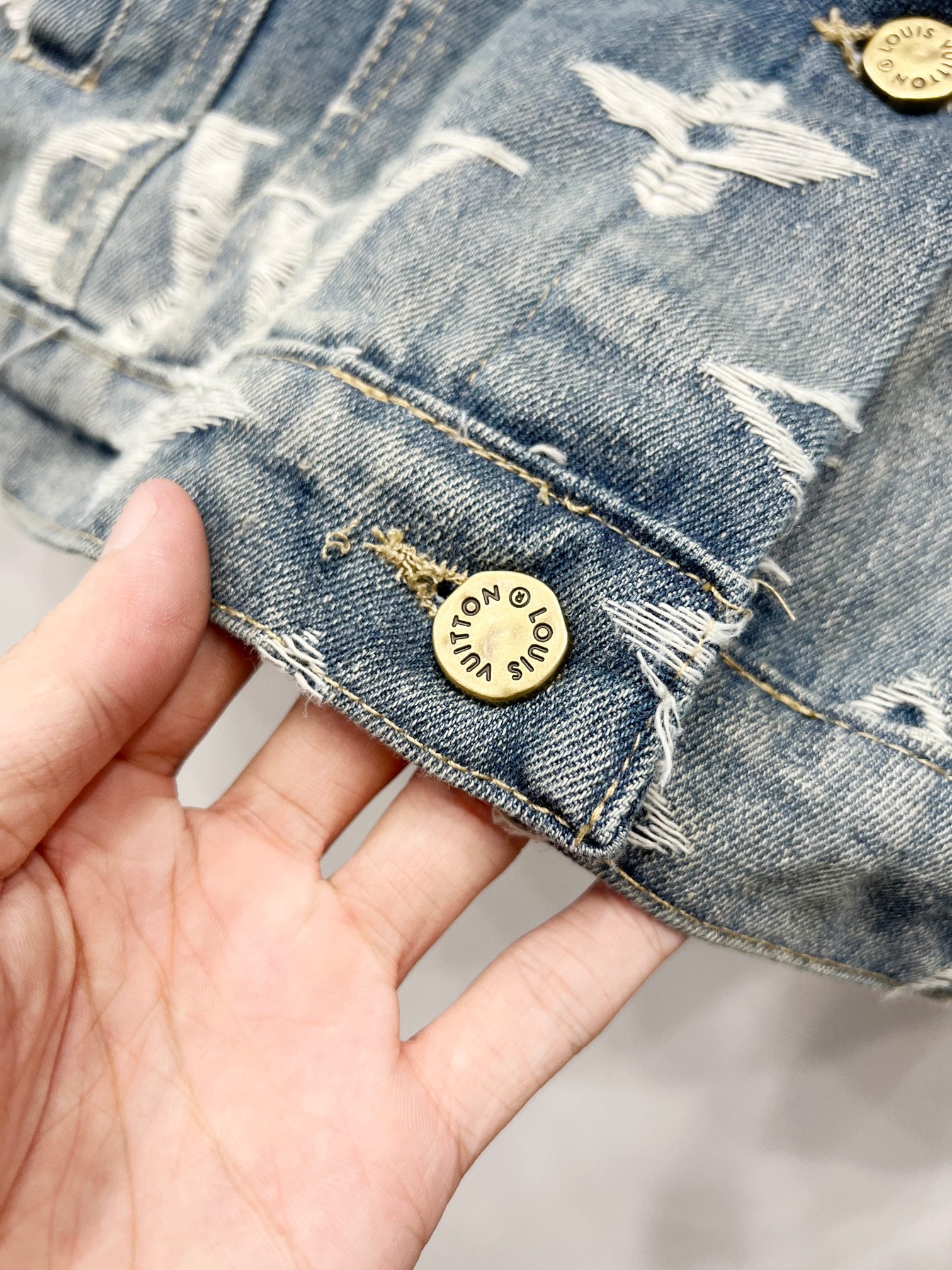 Blue denim jacket cuff with white monogram stitching and round gold logo patch