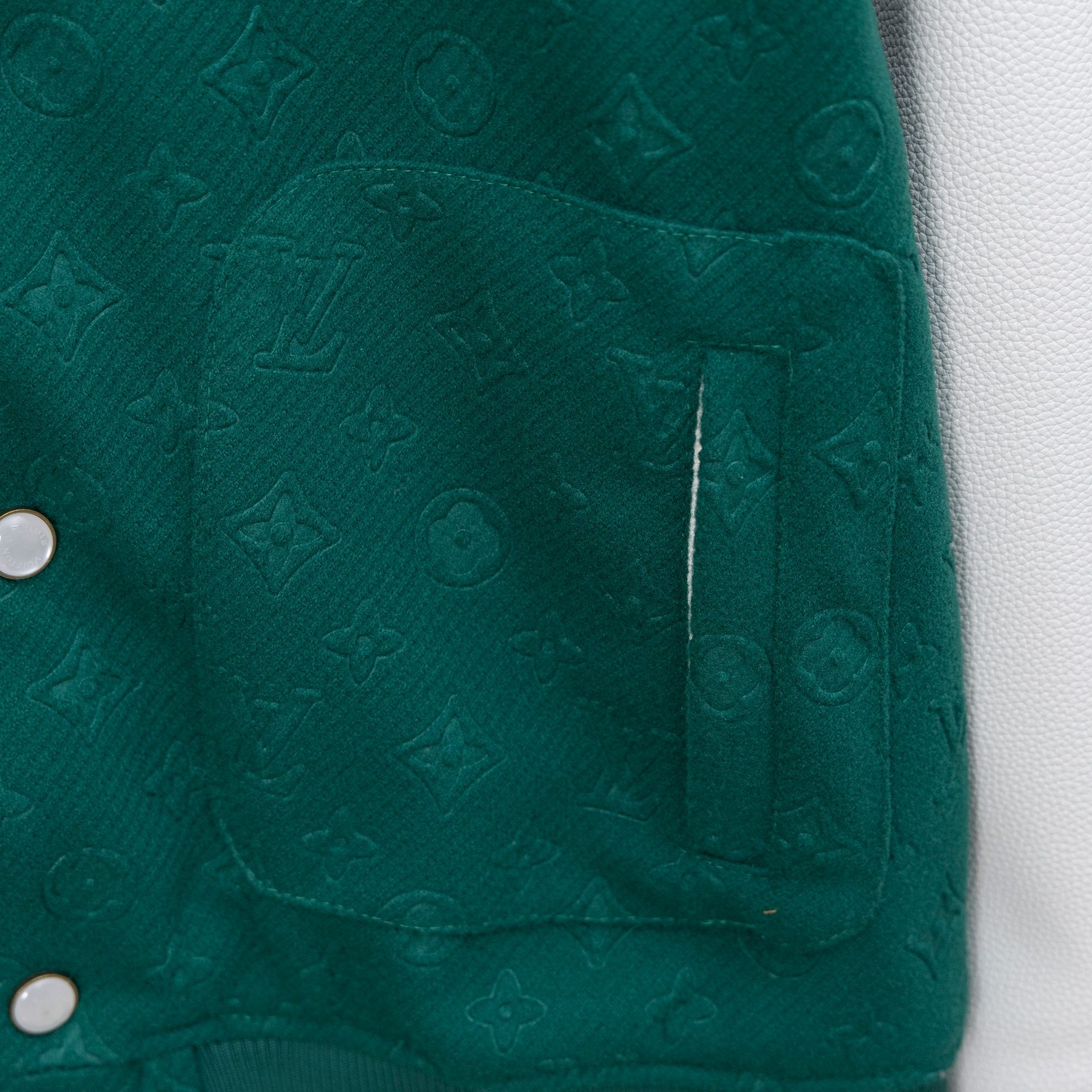 Jacket chest pocket with embossed monogram texture and seam stitching near snap buttons.