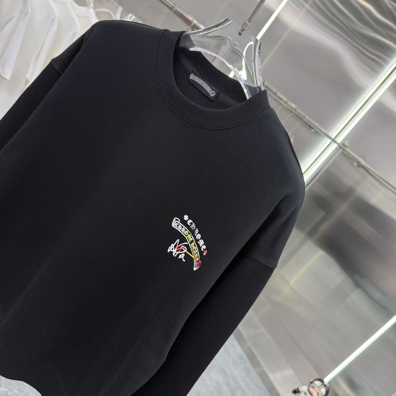 Black crewneck sweatshirt with ribbed collar and multicolor chest logo.