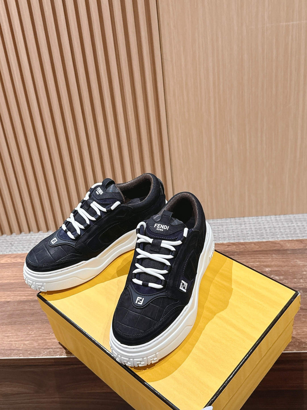 Black Fendi lace-up sneakers on a yellow box, with white platform sole