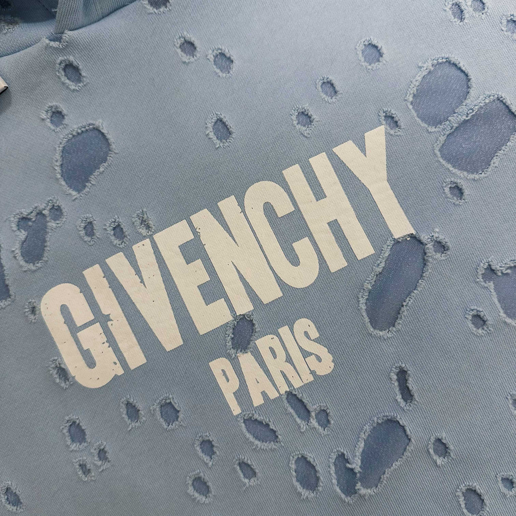 Light blue hoodie fabric close-up with 'GIVENCHY PARIS' text and paw prints