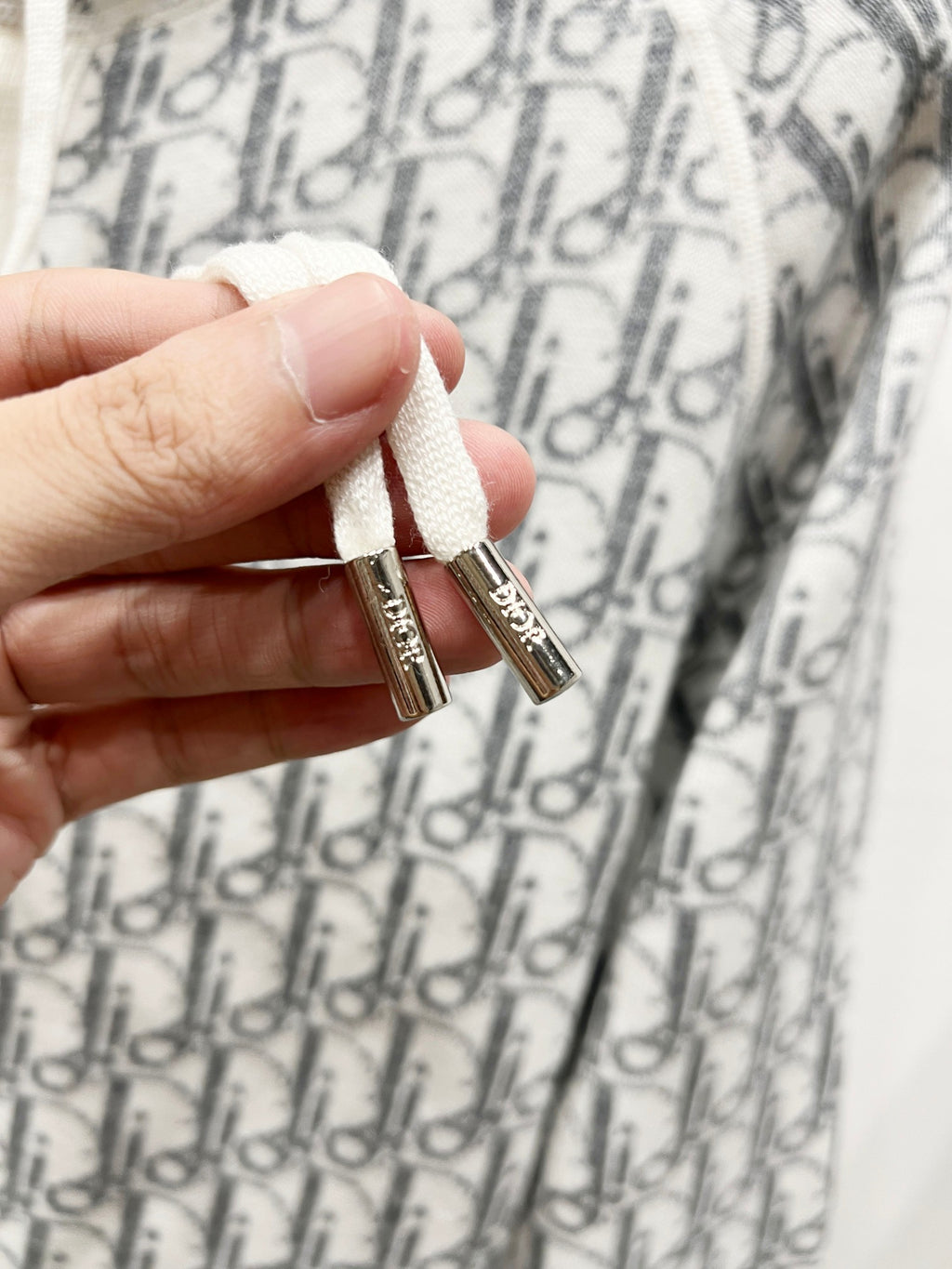 Dior long zip-up hoodie close-up of hand-held zipper pull tabs on monogram print