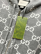 Grey zip-up hoodie fabric close-up with GG-style monogram pattern and hang tag