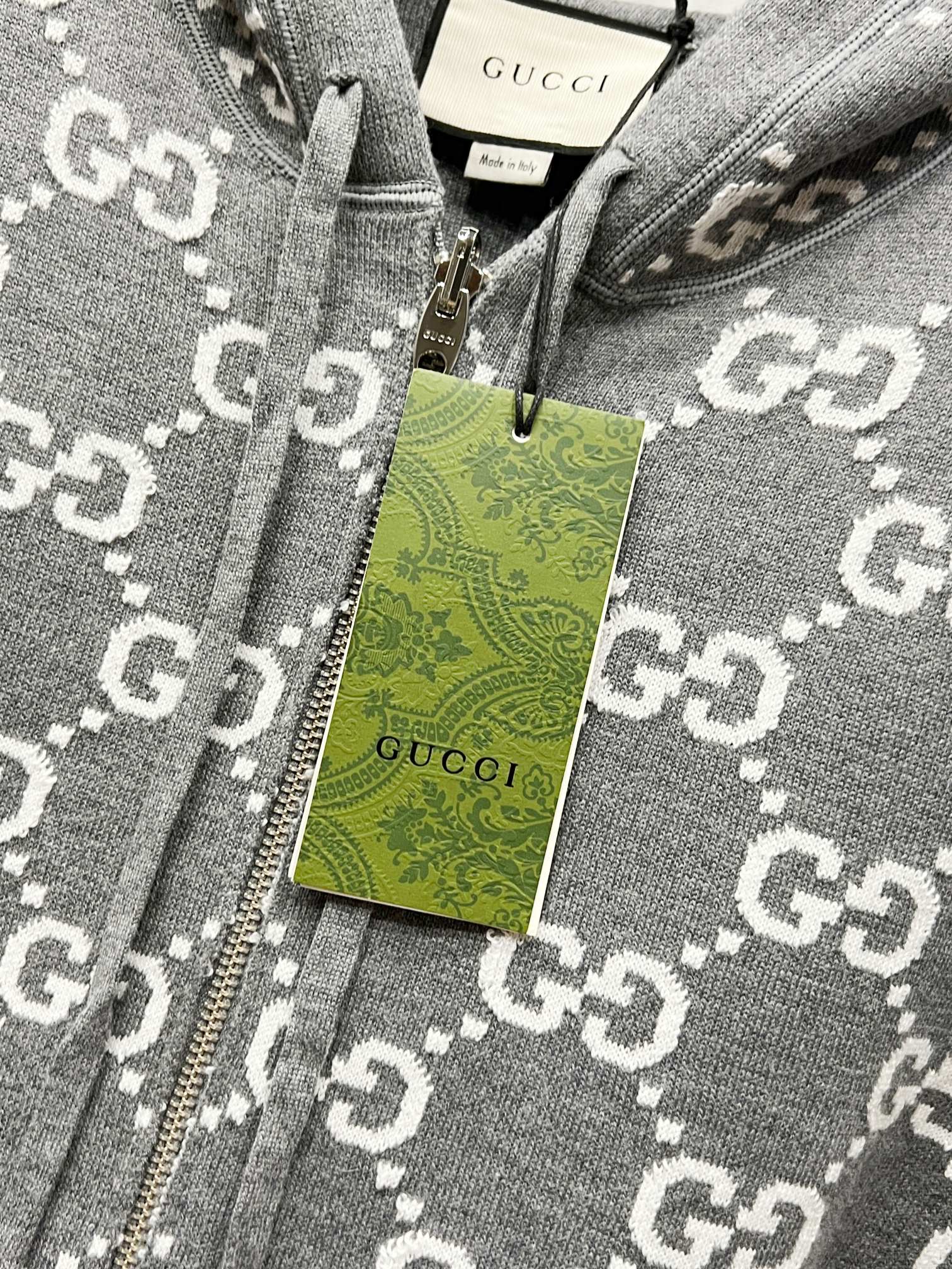 Grey zip-up hoodie fabric close-up with GG-style monogram pattern and hang tag