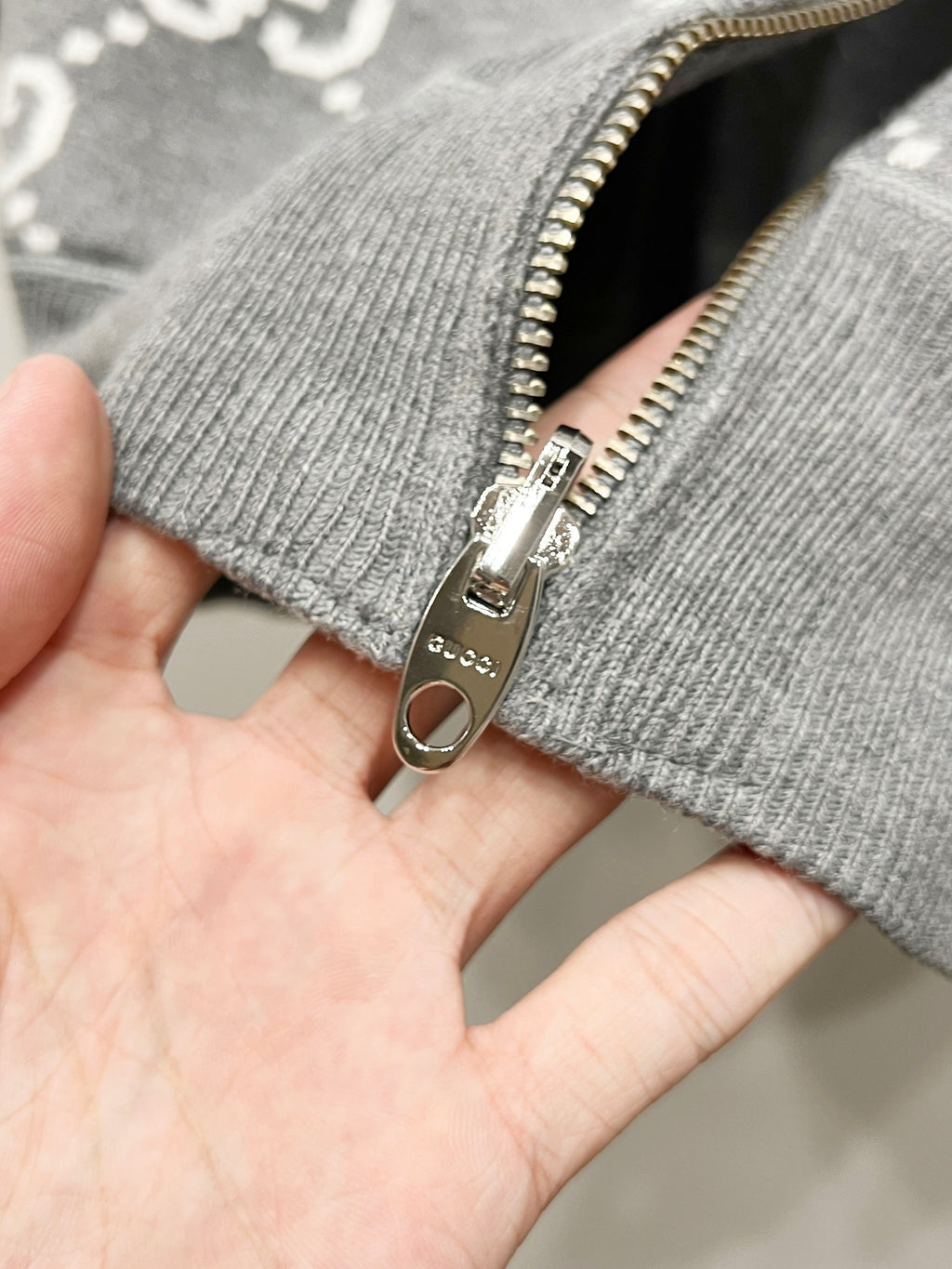 Close-up of grey hoodie zipper pull and ribbed cuff with GG-style pattern