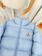 Light blue puffer jacket with high collar, full zip, and Moncler logo patch