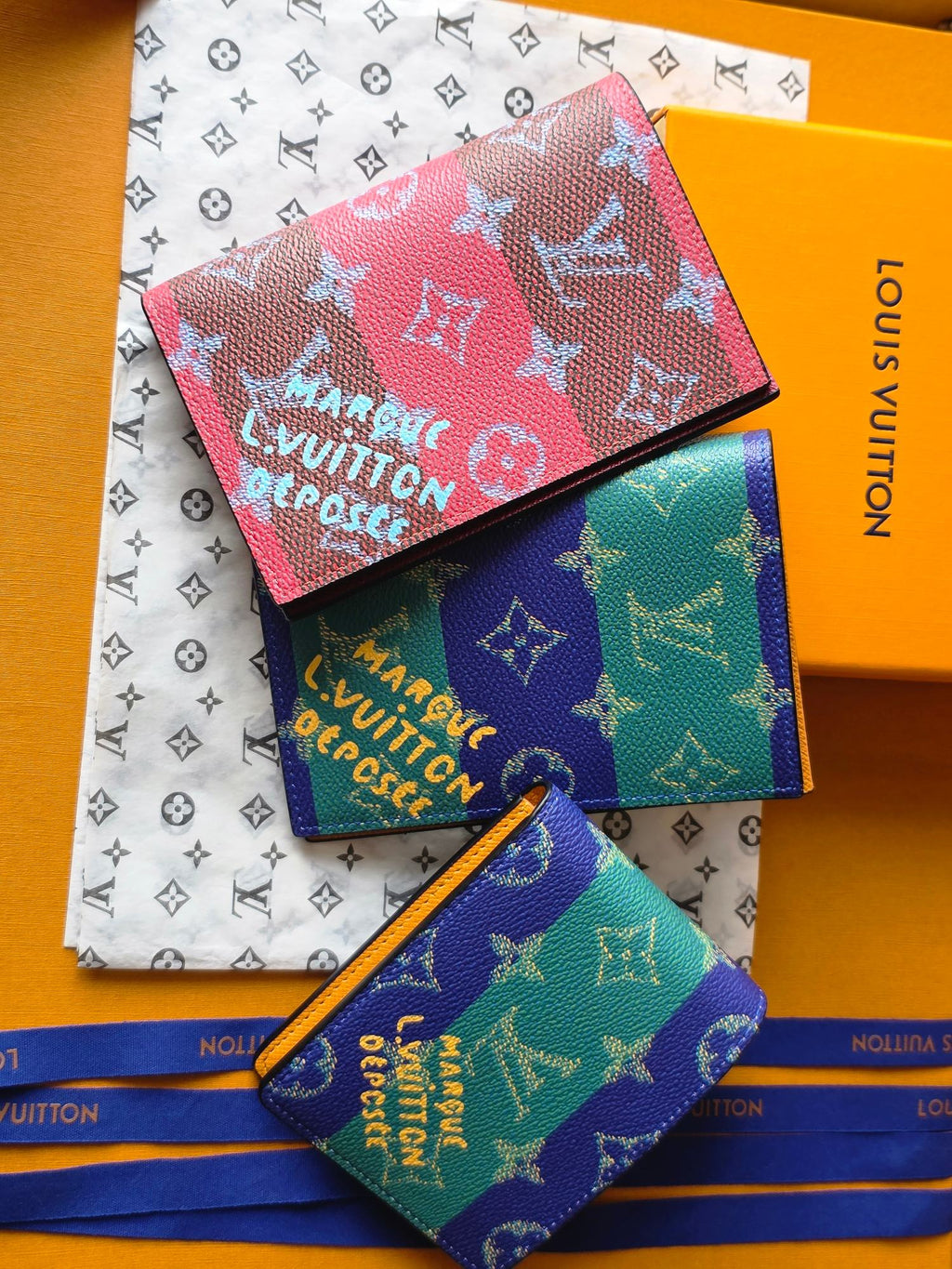 Small bags set in pink, turquoise, and purple monogram prints, stacked