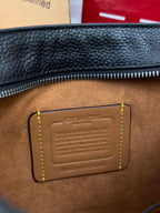 Dark leather crossbody bag detail with embossed logo patch and yellow contrast stitching