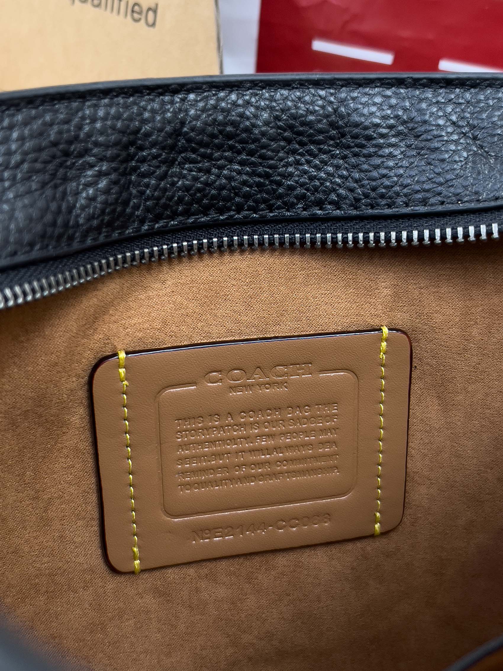 Dark leather crossbody bag detail with embossed logo patch and yellow contrast stitching