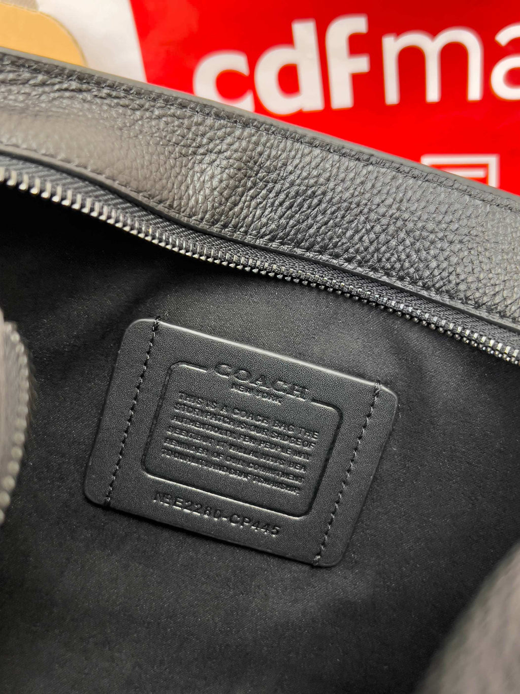 Black leather bag patch with debossed logo and stitched border, close-up