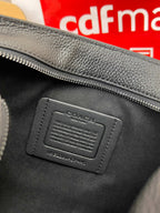 Black leather bag patch with debossed logo and stitched border, close-up