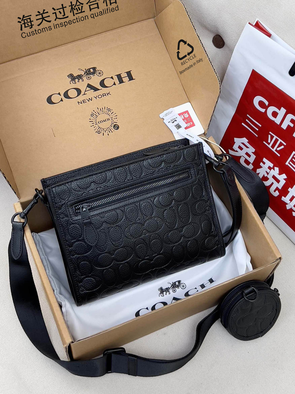 Black COACH crossbody bag with top zip, textured logo pattern, and shoulder strap