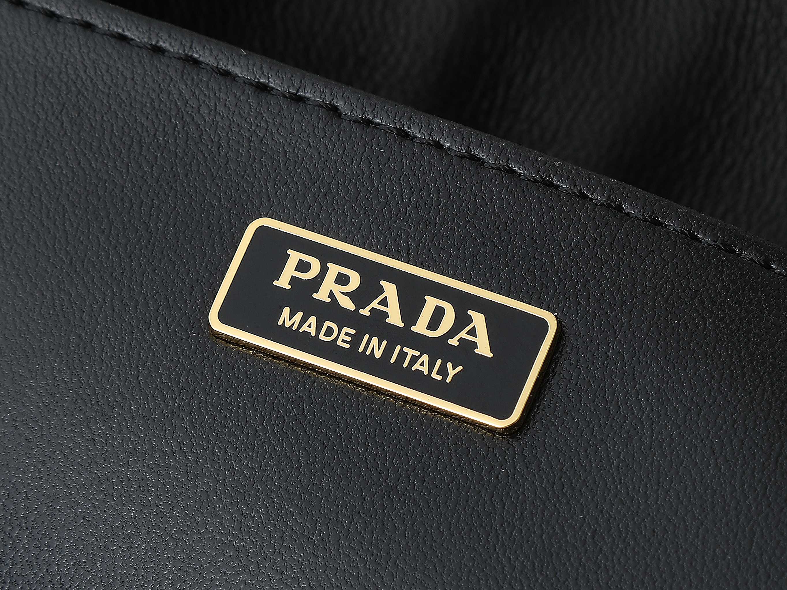 Black leather tag with gold trim reading PRADA and MADE IN ITALY