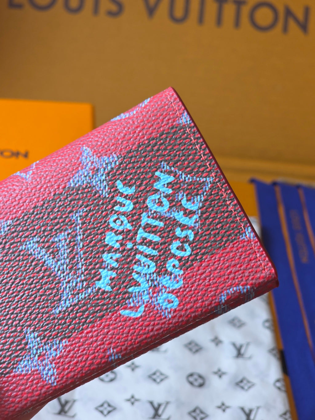 Louis Vuitton wallet with pink textured leather and blue monogram motifs, close-up.