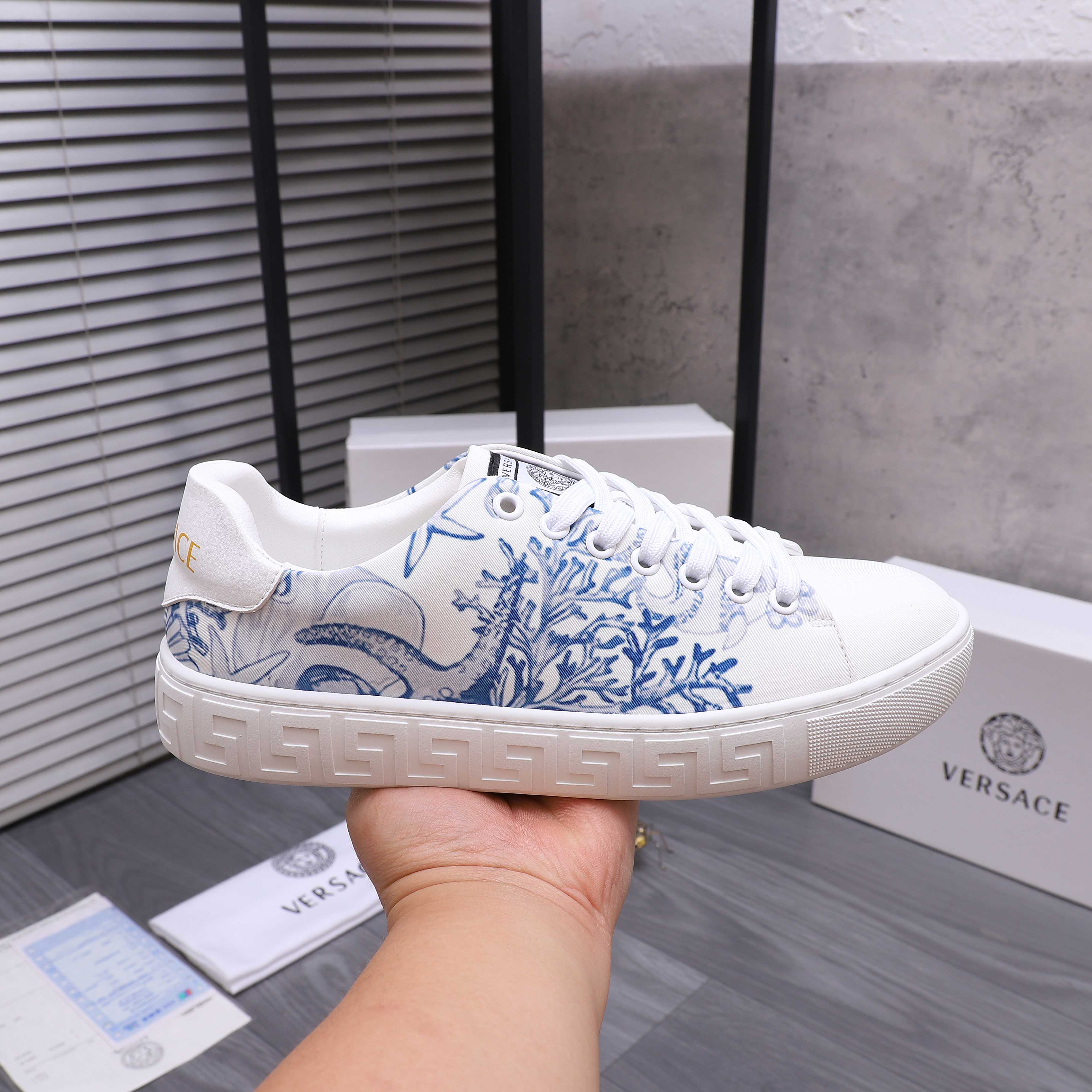White Versace sneakers with blue ornate print, lace-up, held up for close view.