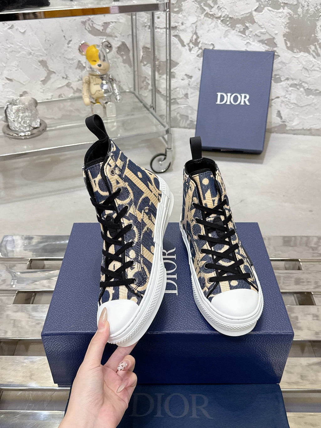 Dior unisex high-top sneakers in blue and beige with black laces, held in hand