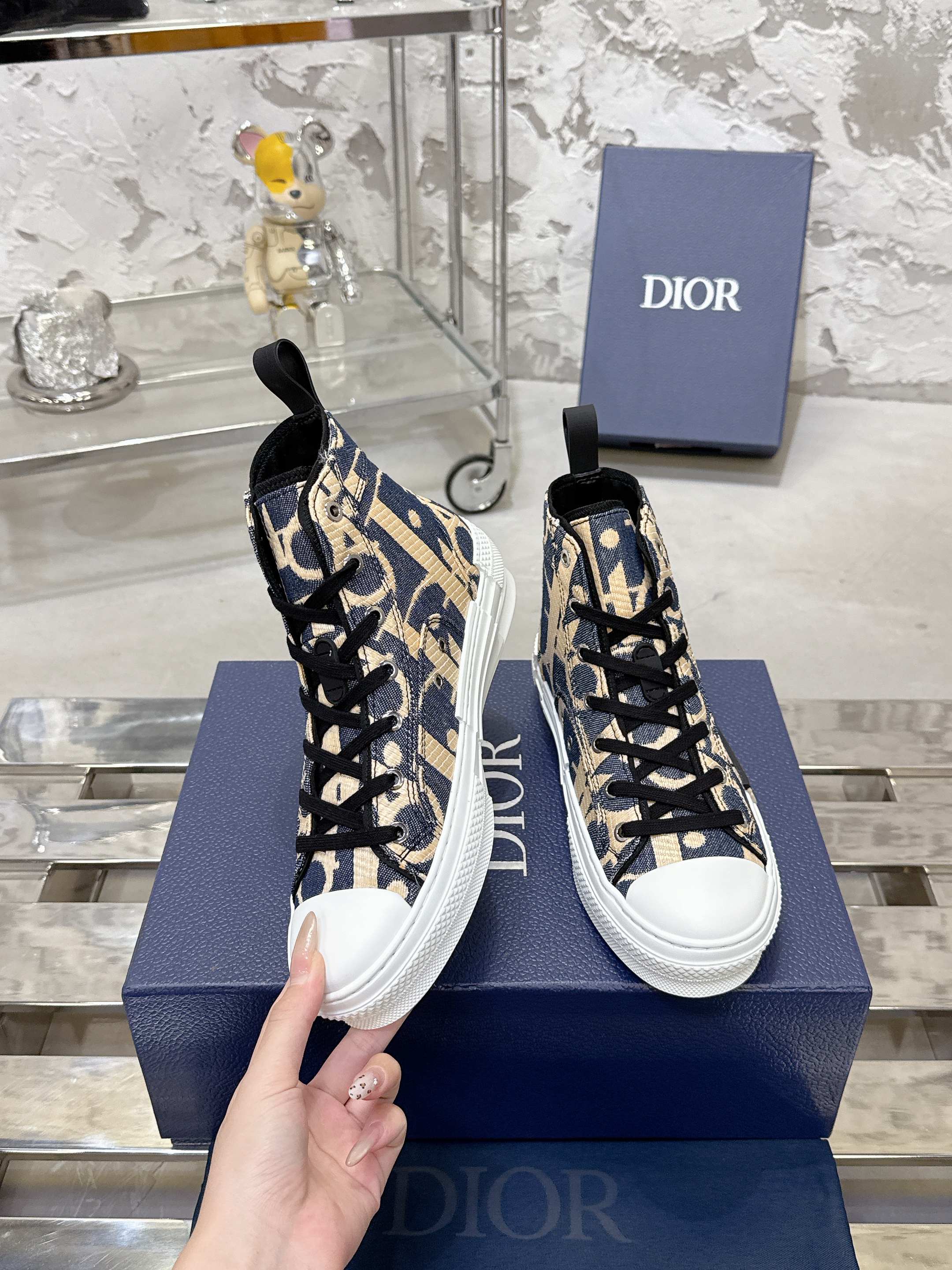 Dior unisex high-top sneakers in blue and beige with black laces, held in hand