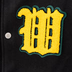 Yellow graffiti-style letter patch with green border on black varsity jacket.