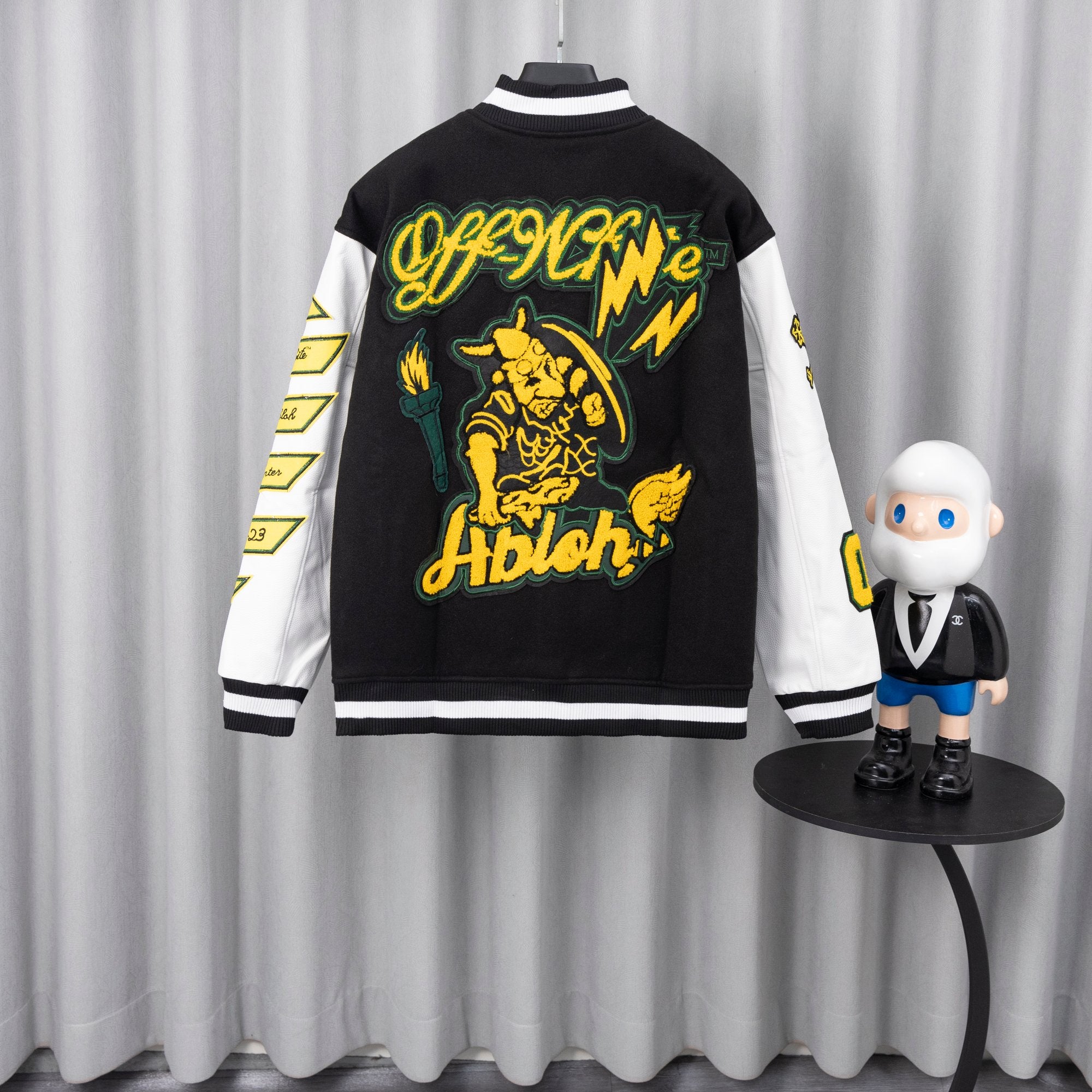 Back varsity jacket with large yellow cat graphic and green outline lettering.