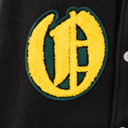 Yellow letter patch with green border on black varsity jacket.
