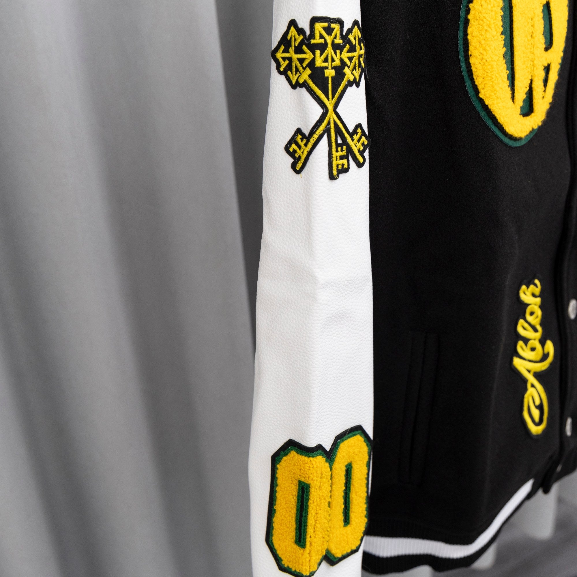 Sleeve of black-and-white varsity jacket with yellow logo print and geometric motif.