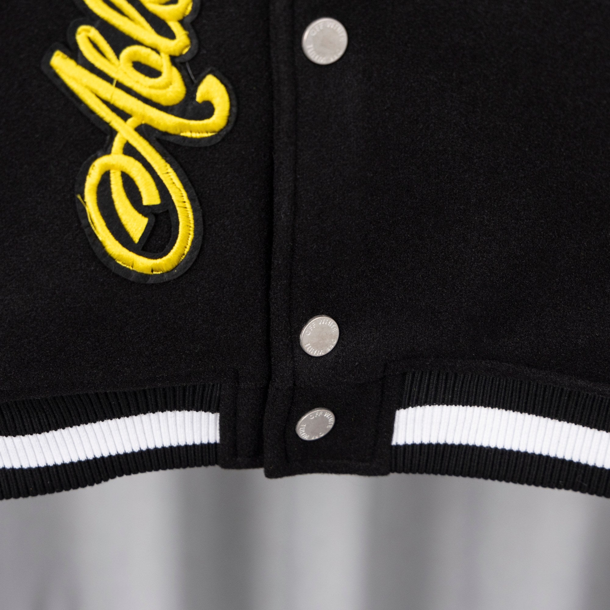 Hem and snap placket of black varsity jacket with white striped ribbed cuffs.