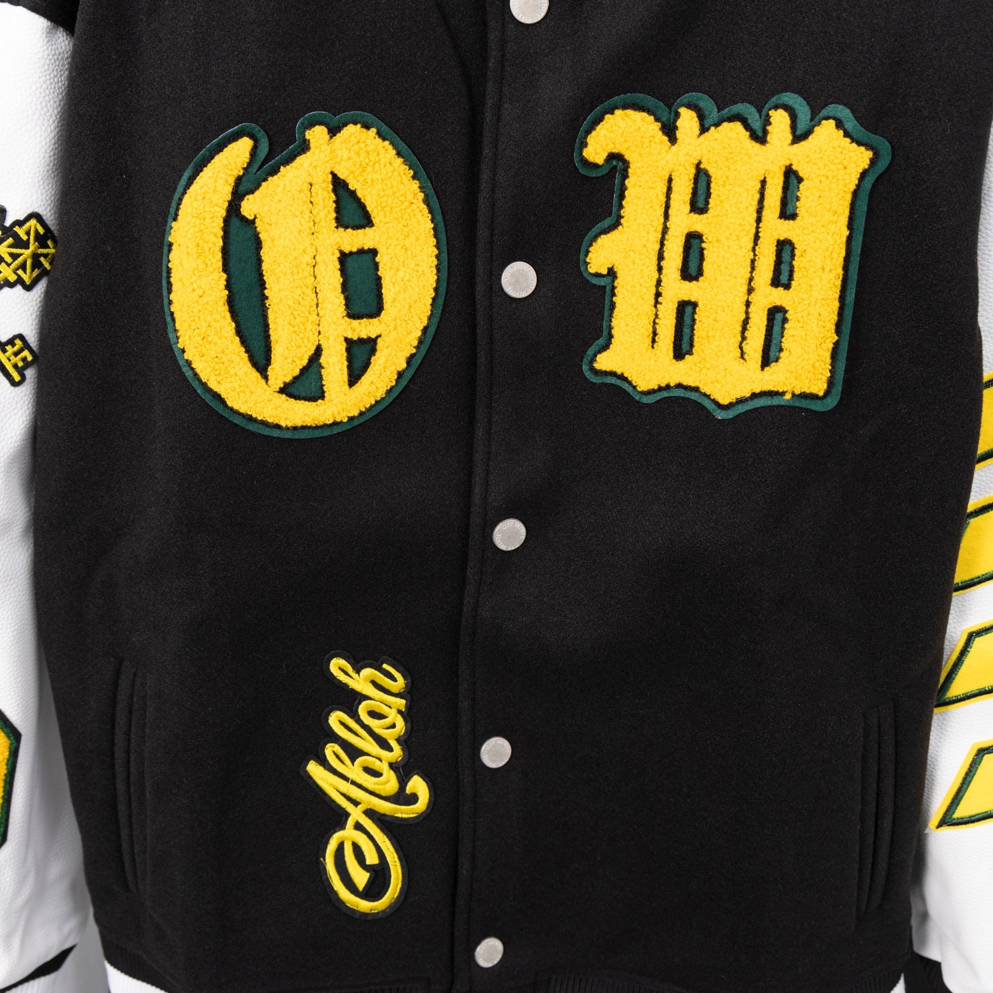 Black front varsity jacket with yellow logo patches and snap-button placket.