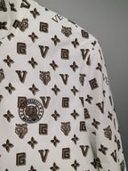 White jacket fabric close-up with repeating dark monogram symbols and crest details.