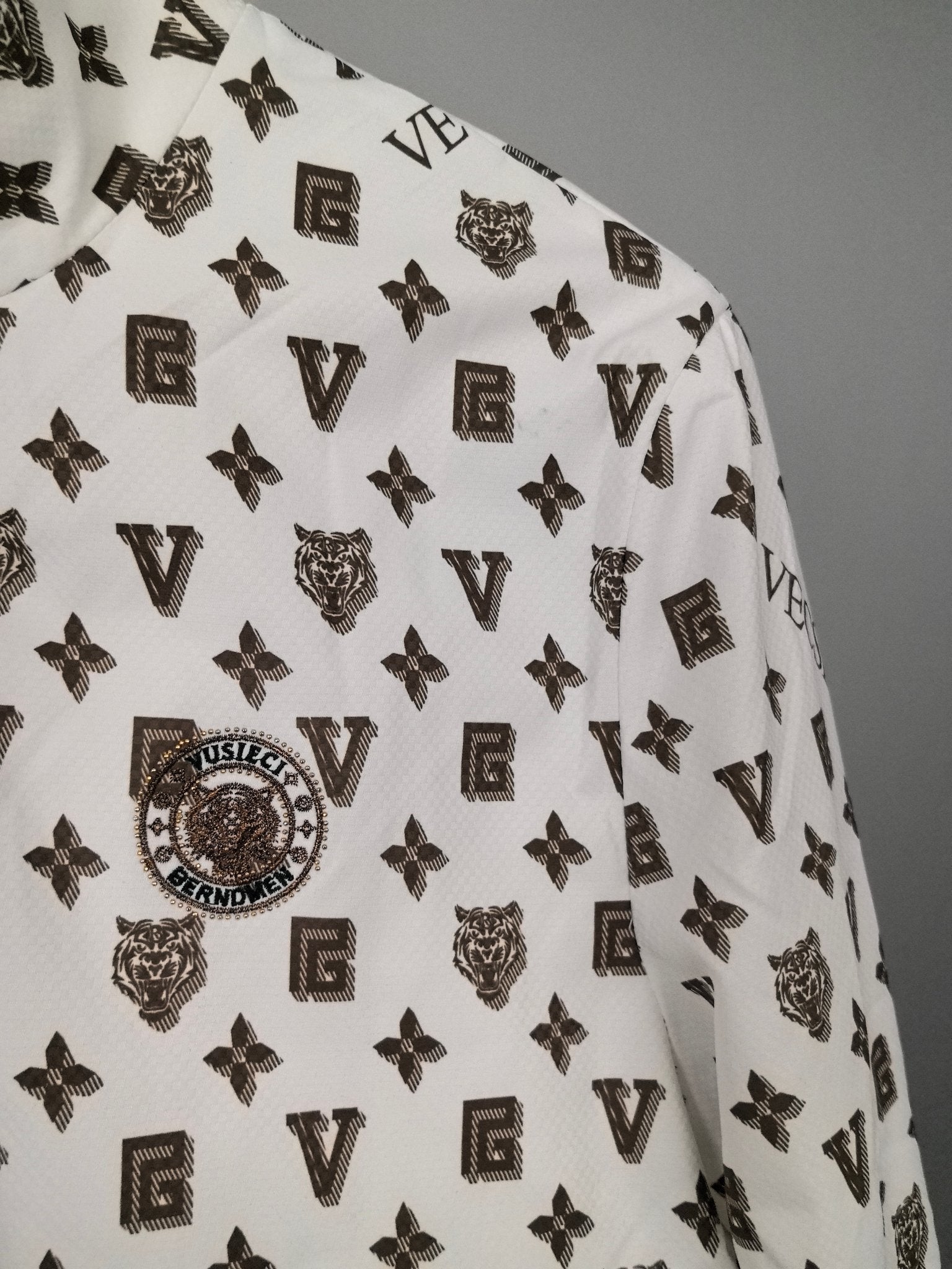 White jacket fabric close-up with repeating dark monogram symbols and crest details.
