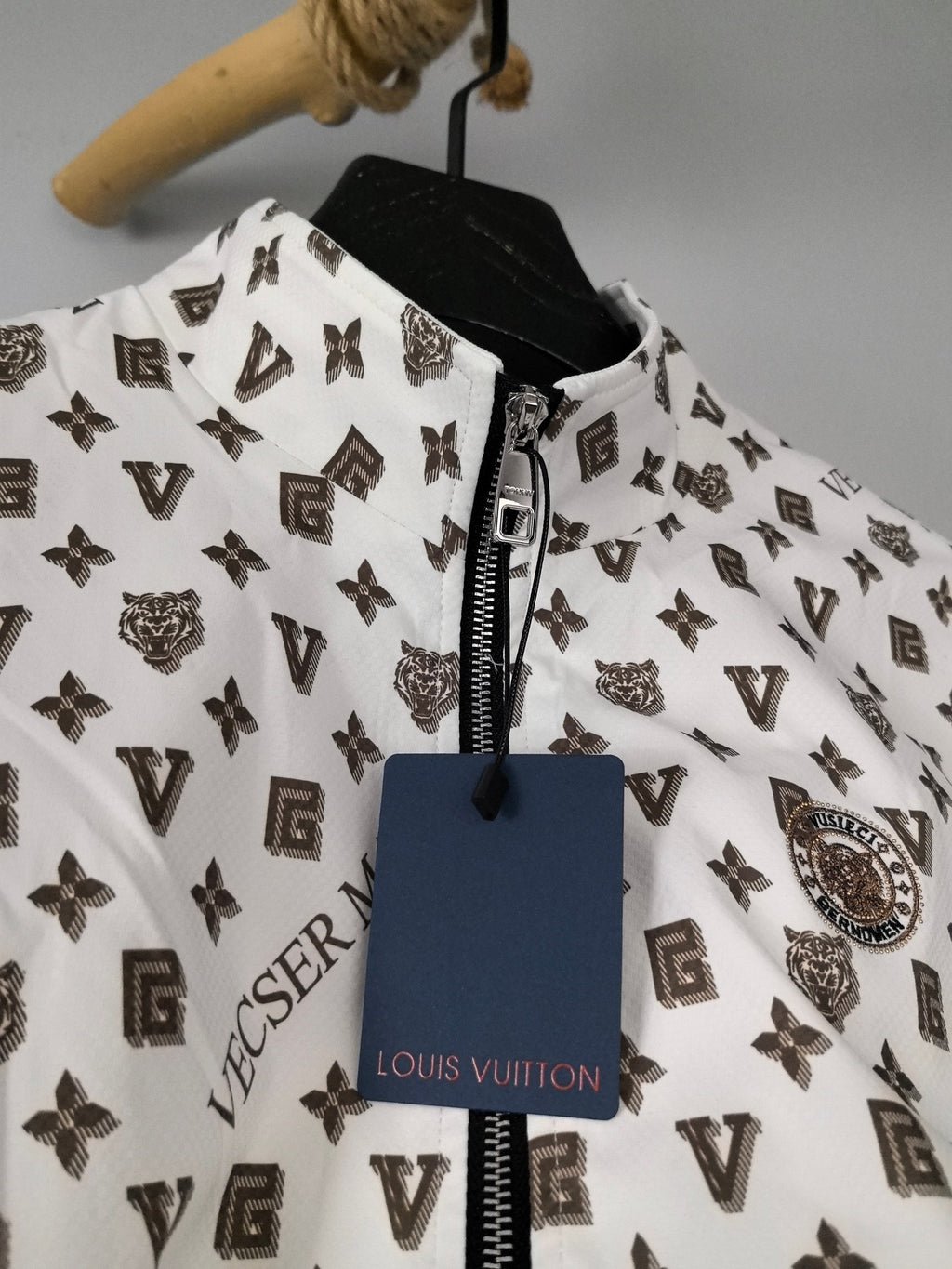 Zip-front jacket close-up in white with dark monogram print and metal zipper pull.