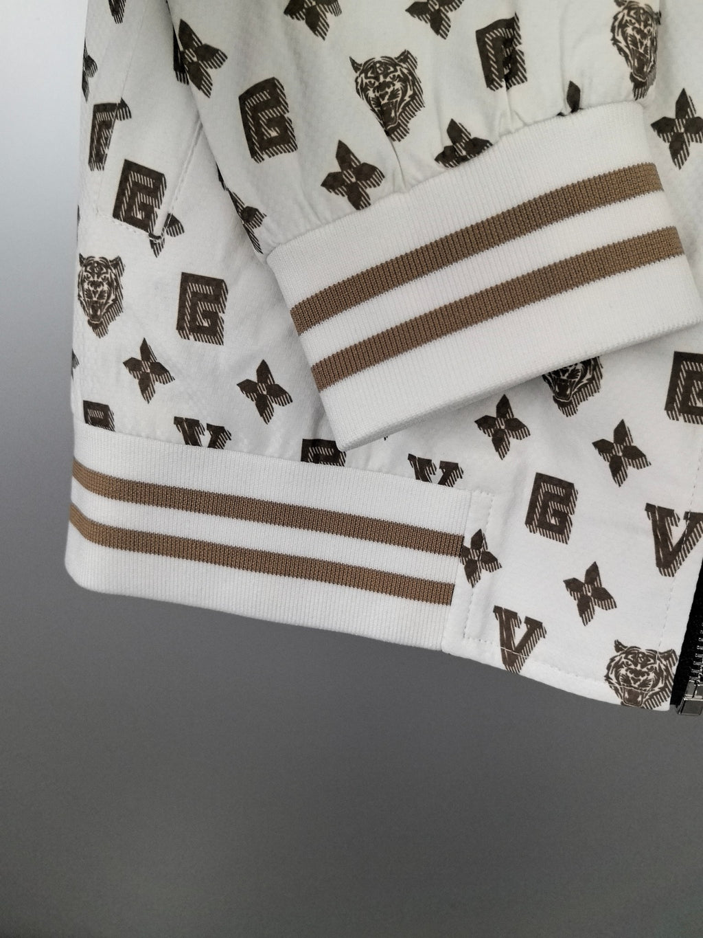 White jacket sleeve cuff with dark monogram print and tan-striped ribbed trim.