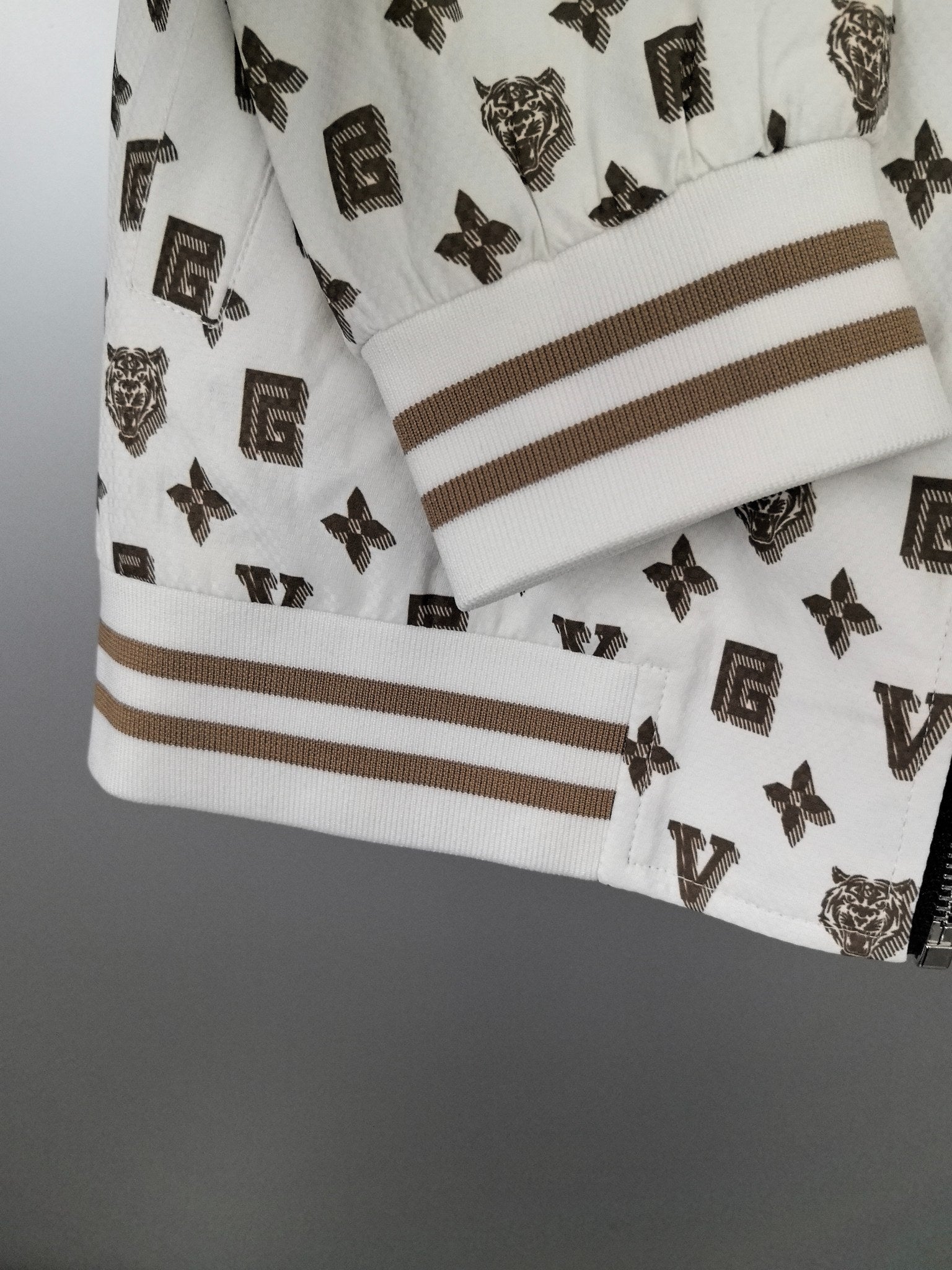 White jacket sleeve cuff with dark monogram print and tan-striped ribbed trim.