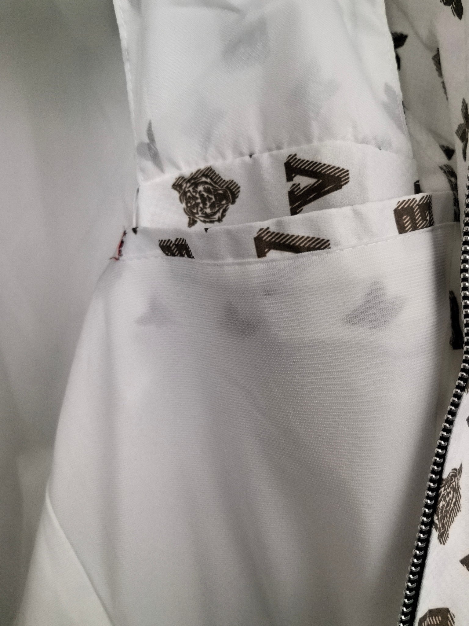 White jacket hem area with dark monogram print and ribbed trim near zipper opening.