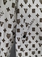 White jacket front close-up with dark monogram pattern and small round snap at placket.