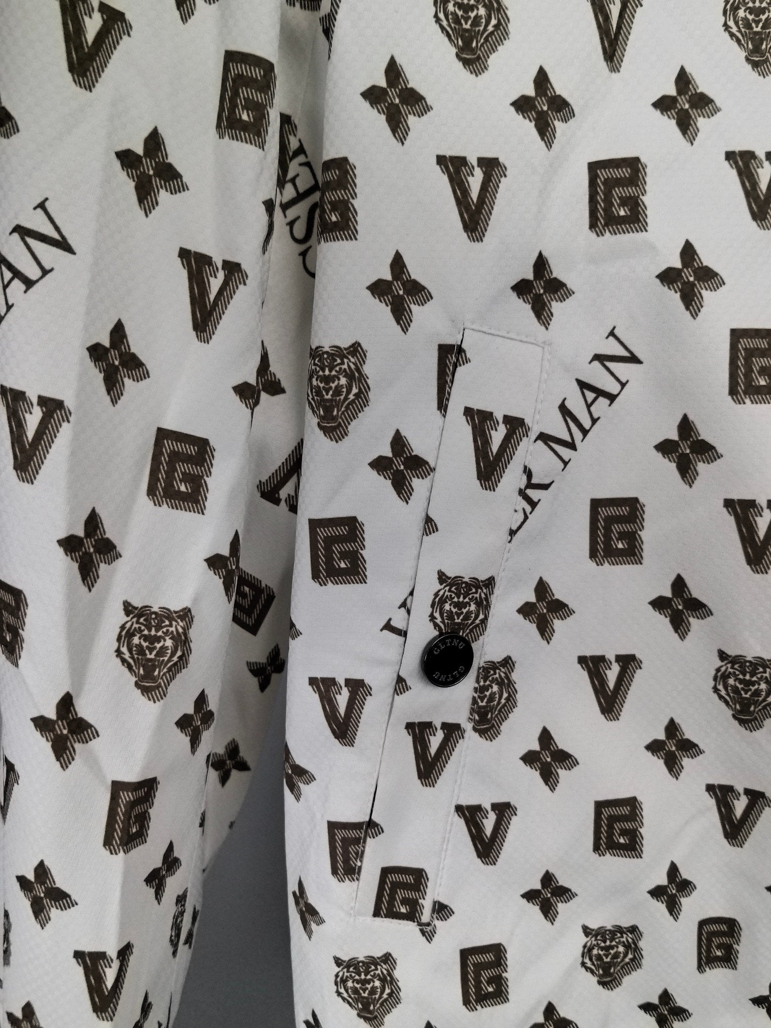 White jacket front close-up with dark monogram pattern and small round snap at placket.