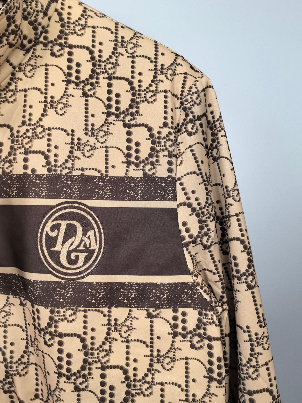 Beige jacket with dark stripe and circular logo patch on chest, close-up