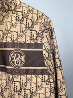 Beige jacket with dark stripe and circular logo patch on chest, close-up