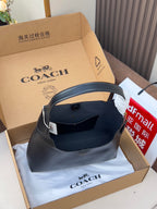 Dark blue hobo shoulder bag with white tag and gold logo, resting in box