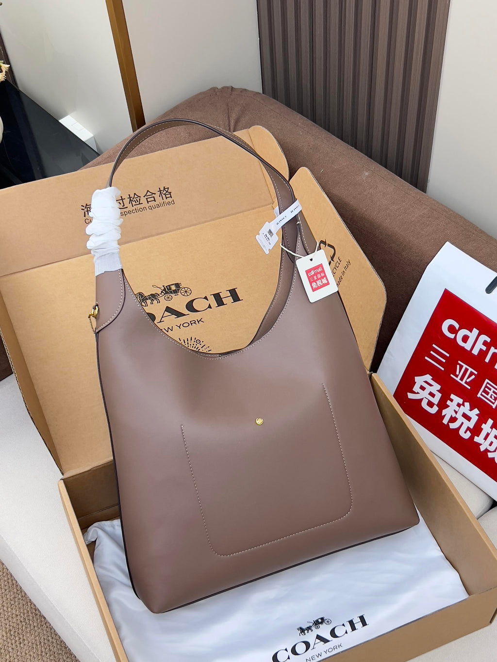 Taupe leather handbag with top handles, shown in a gift box on padding.
