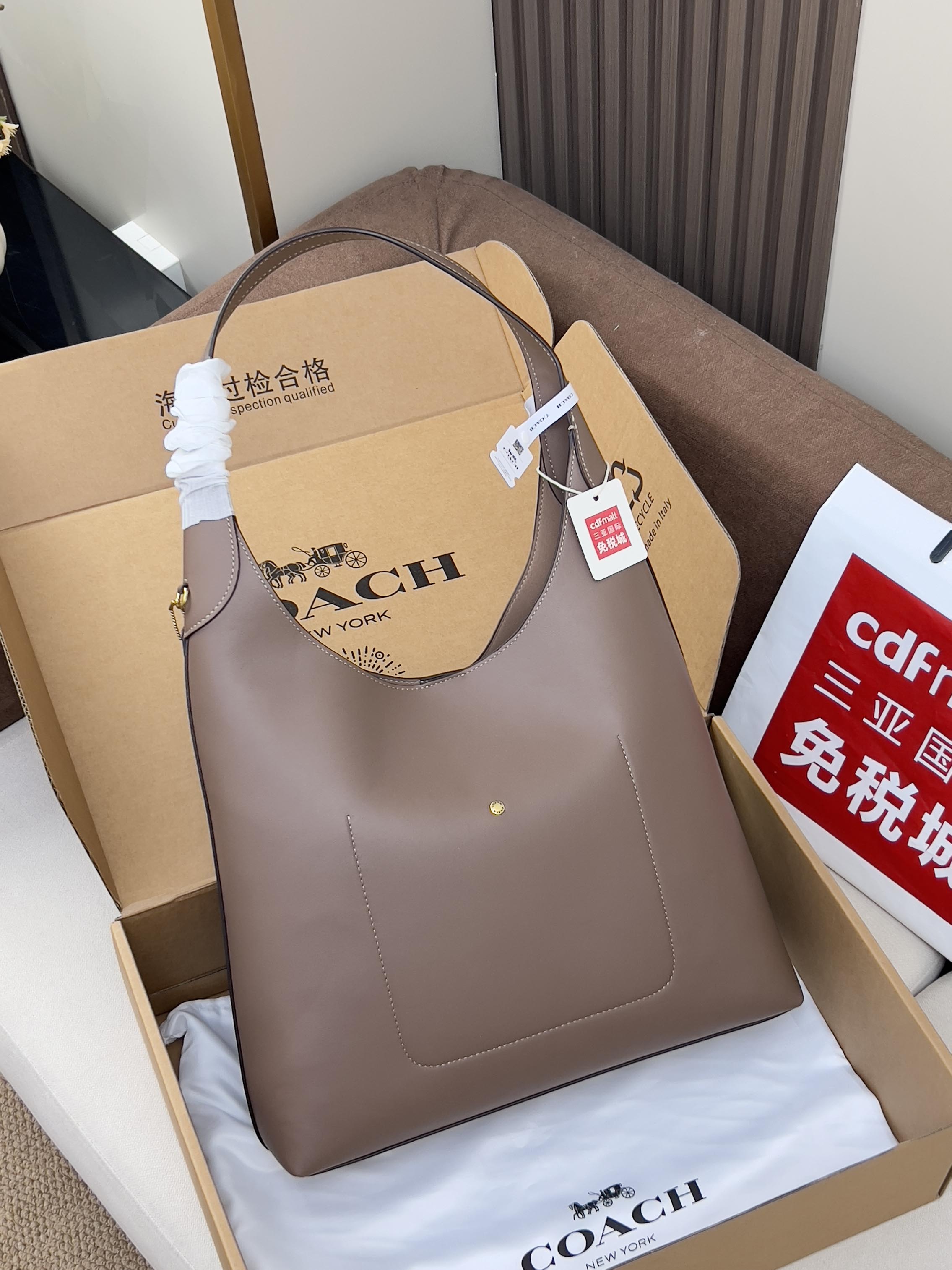 Taupe leather handbag with top handles, shown in a gift box on padding.