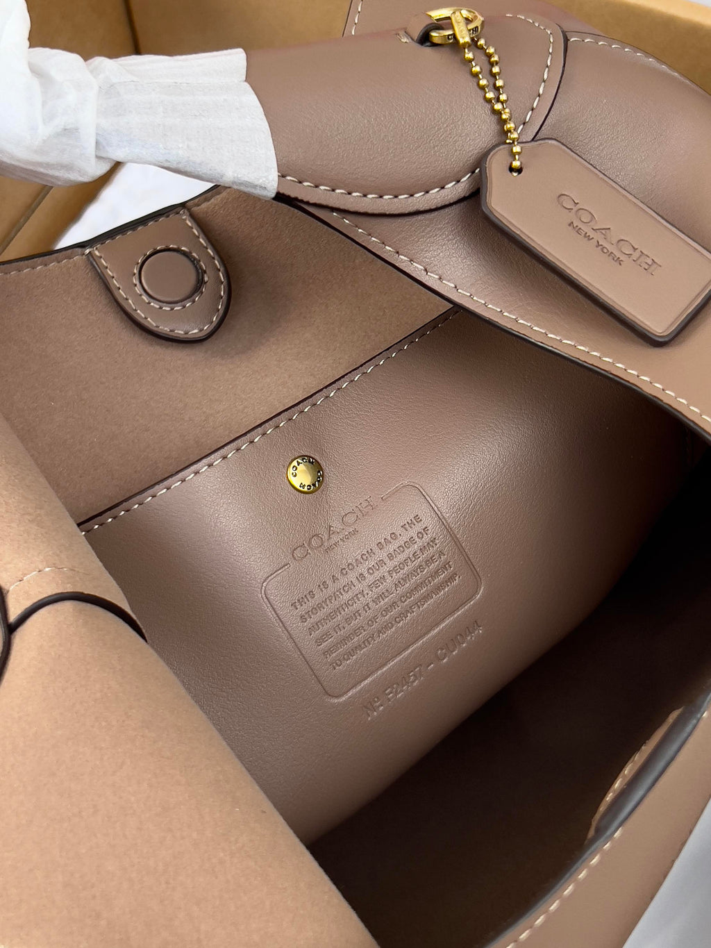 Taupe leather handbag detail with gold chain key holder and stitched trim.