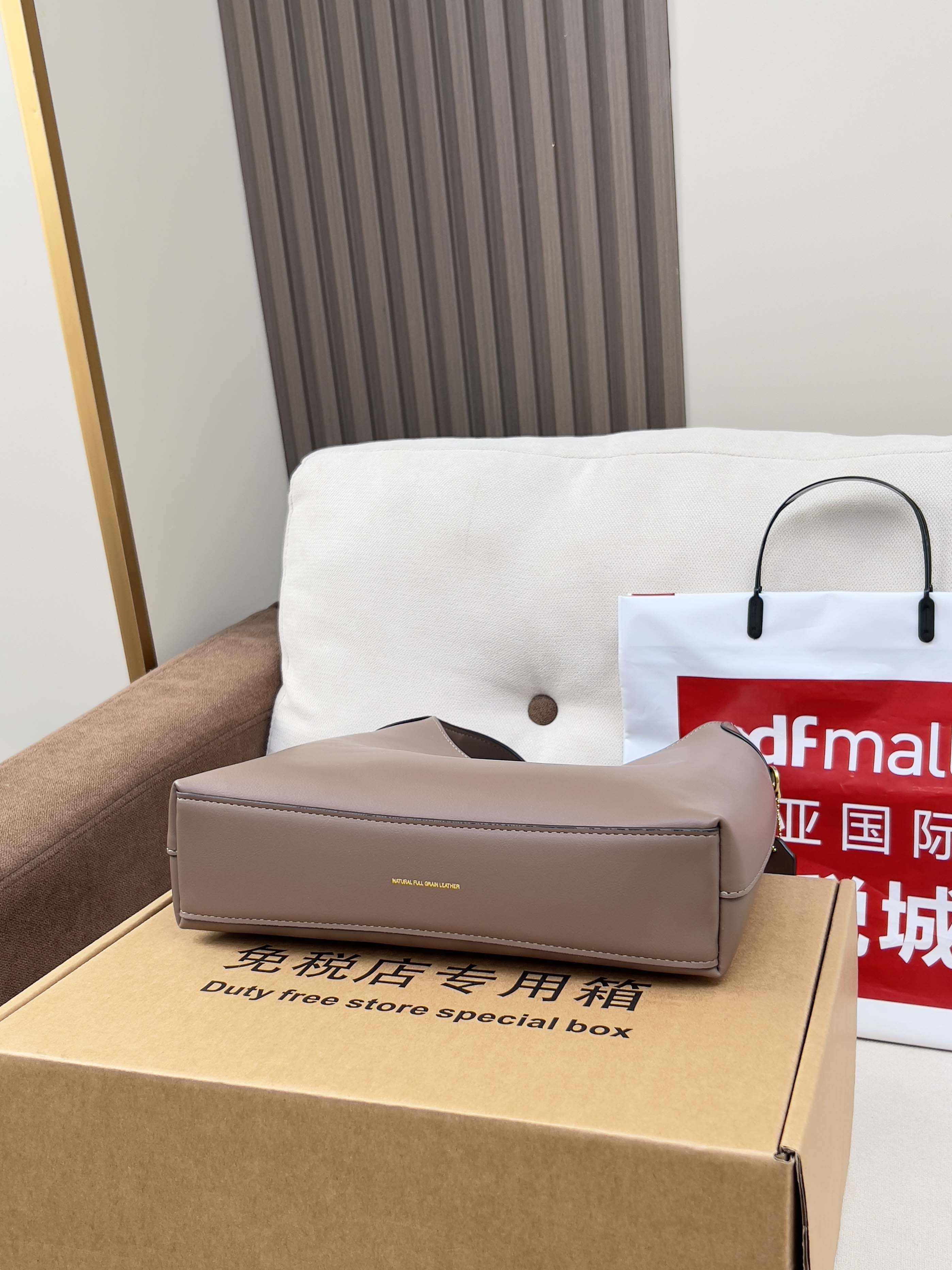 Taupe handbag and retail box on sofa