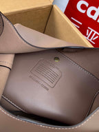 Taupe handbag close-up with embossed brand label and gold-tone hardware